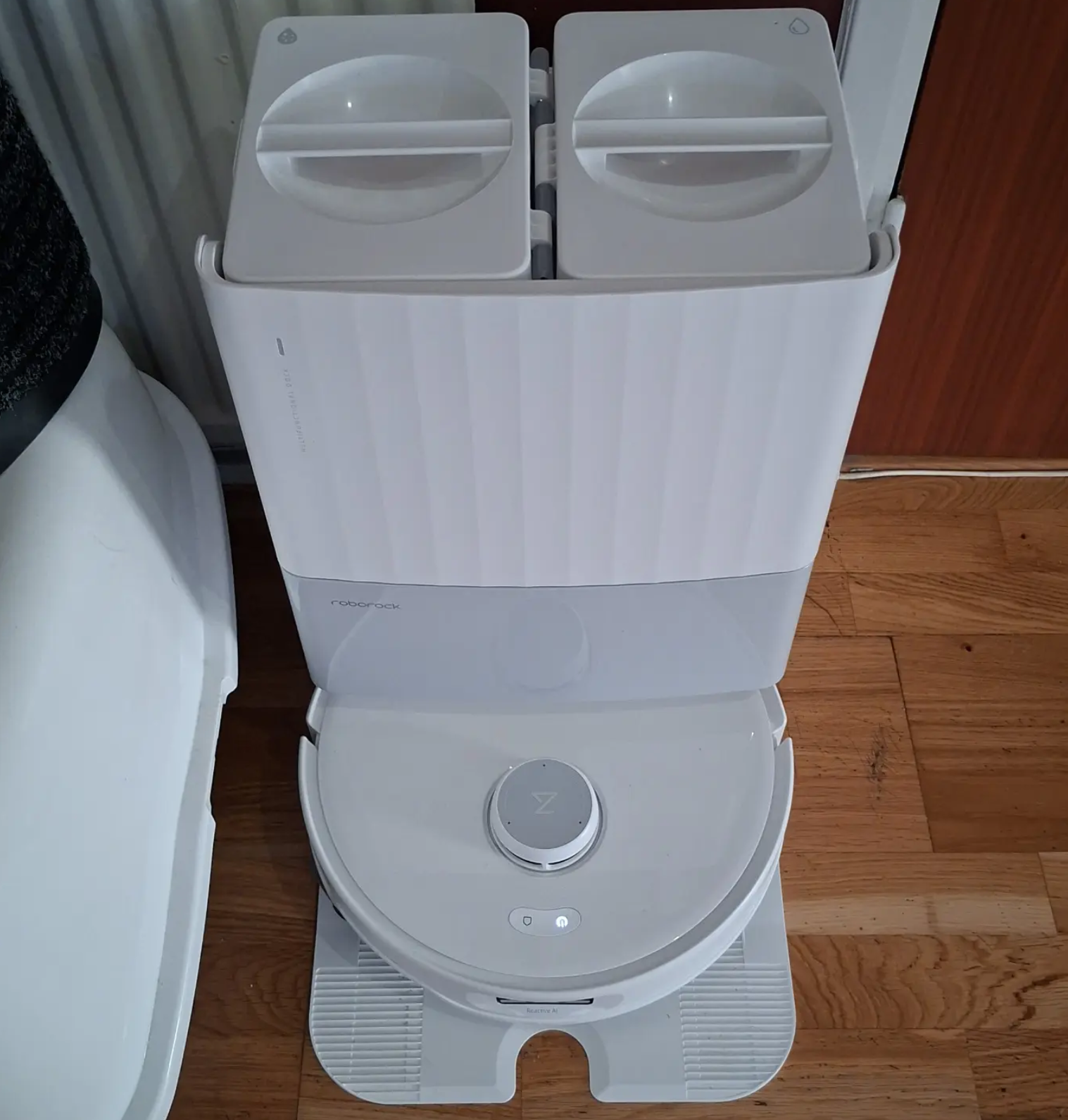 Vit Roborock-robotdammsugare vid sin laddstation på ett trägolv
